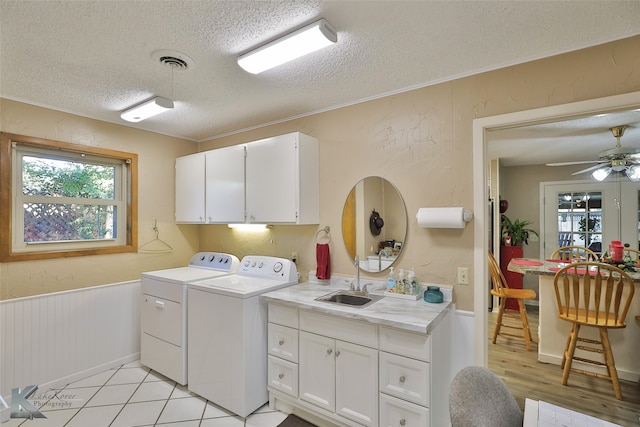 clothes washing area with sink, cabinets, a textured ceiling, washer and dryer, and light wood-type flooring