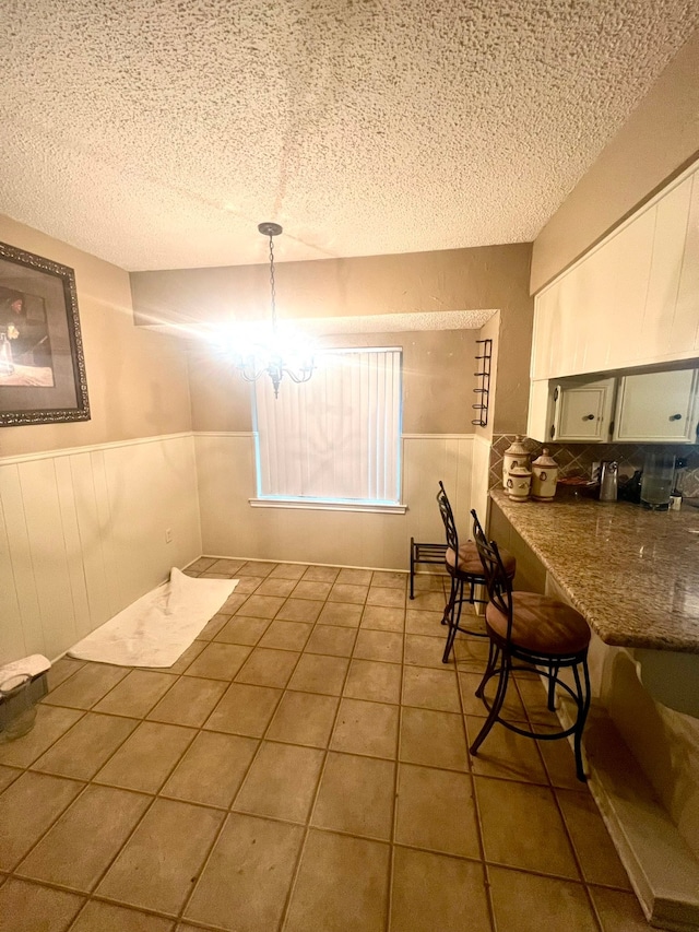 unfurnished dining area with a chandelier, a textured ceiling, and tile patterned flooring