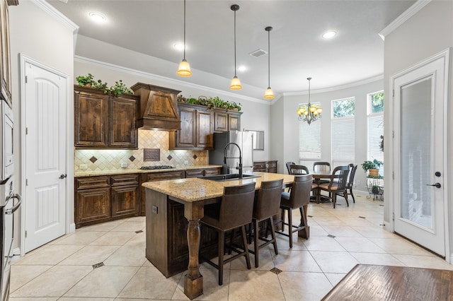 kitchen featuring a breakfast bar, an island with sink, pendant lighting, stainless steel appliances, and light stone countertops