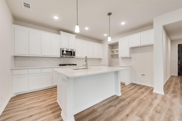 kitchen with decorative light fixtures, light wood finished floors, stainless steel microwave, visible vents, and a sink