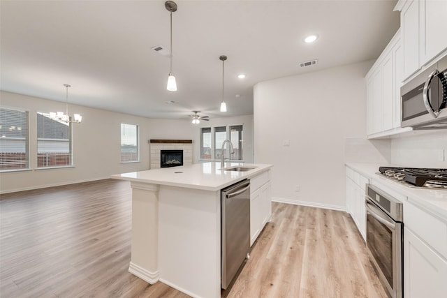 kitchen featuring visible vents, a glass covered fireplace, open floor plan, stainless steel appliances, and a sink