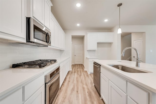 kitchen with a sink, white cabinetry, appliances with stainless steel finishes, light wood-type flooring, and pendant lighting