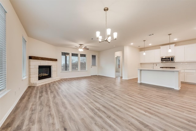 unfurnished living room with light wood-style floors, visible vents, a stone fireplace, and baseboards