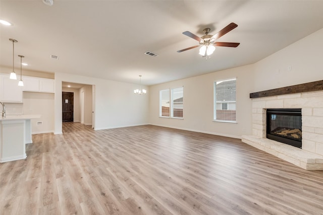 unfurnished living room with light wood-style floors, visible vents, a fireplace, and ceiling fan with notable chandelier