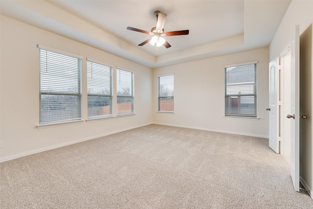 spare room with a ceiling fan, a raised ceiling, light colored carpet, and baseboards