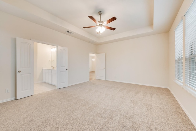 unfurnished bedroom with light carpet, a tray ceiling, visible vents, and baseboards