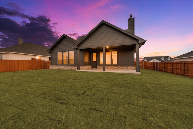 back of property featuring a fenced backyard, brick siding, a yard, a chimney, and a patio area