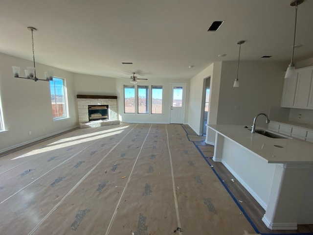 unfurnished living room featuring ceiling fan with notable chandelier, a stone fireplace, sink, and a wealth of natural light