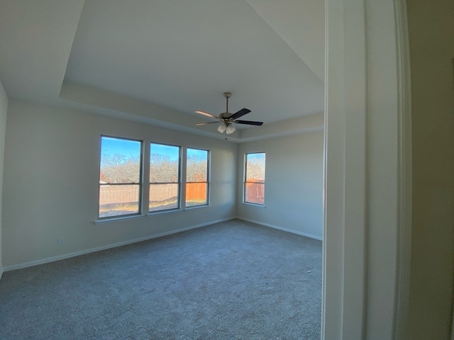 carpeted empty room with a raised ceiling and ceiling fan