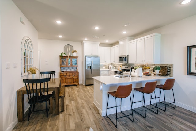 kitchen with white cabinets, sink, light hardwood / wood-style floors, kitchen peninsula, and stainless steel appliances