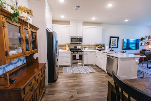 kitchen featuring stainless steel appliances, dark hardwood / wood-style flooring, kitchen peninsula, a breakfast bar, and white cabinets