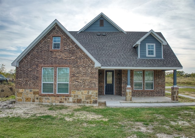 view of front of home featuring stone siding, a porch, roof with shingles, a front yard, and brick siding