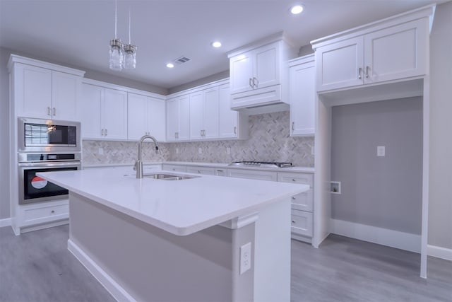 kitchen with decorative light fixtures, light hardwood / wood-style floors, white cabinetry, and a kitchen island with sink