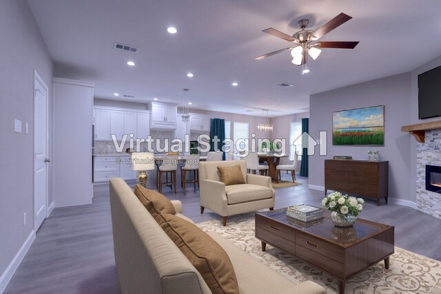 living area featuring visible vents, light wood-style flooring, a fireplace, recessed lighting, and ceiling fan with notable chandelier