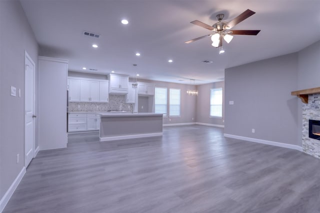 unfurnished living room with visible vents, baseboards, ceiling fan, a stone fireplace, and wood finished floors