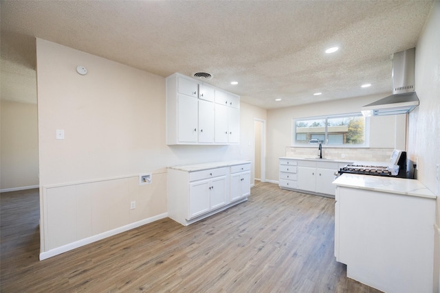 kitchen with range, sink, wall chimney exhaust hood, a textured ceiling, and white cabinetry