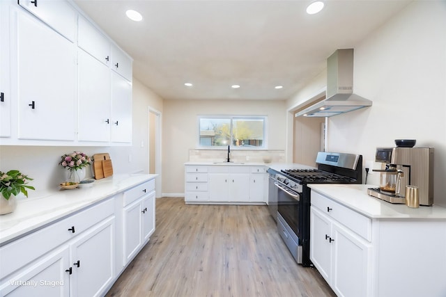 kitchen with sink, wall chimney range hood, stainless steel gas stove, light hardwood / wood-style floors, and white cabinetry