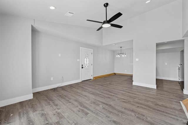 unfurnished living room with wood-type flooring, ceiling fan with notable chandelier, and high vaulted ceiling