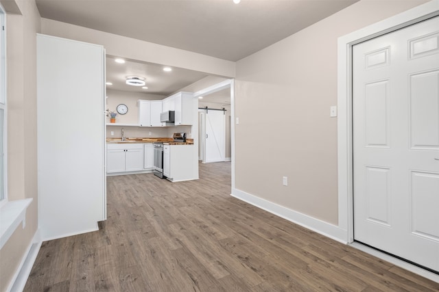 kitchen featuring wood counters, sink, a barn door, stainless steel range, and white cabinetry