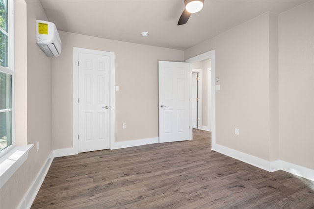 unfurnished bedroom featuring an AC wall unit, multiple windows, dark wood-type flooring, and ceiling fan