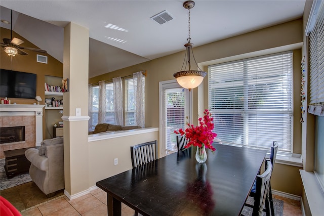 dining space featuring a tile fireplace, ceiling fan, light tile patterned floors, and vaulted ceiling