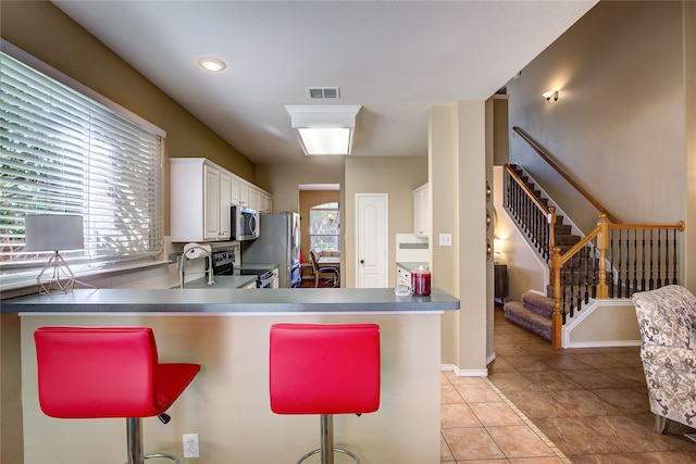 kitchen with stainless steel appliances, light tile patterned floors, kitchen peninsula, a kitchen bar, and white cabinets