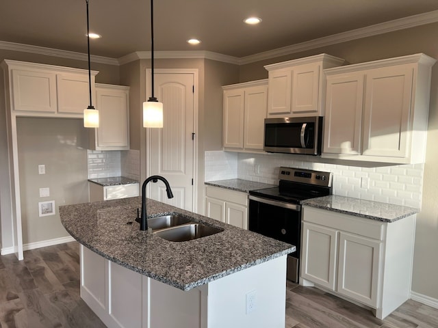 kitchen with white cabinets, appliances with stainless steel finishes, decorative light fixtures, an island with sink, and sink