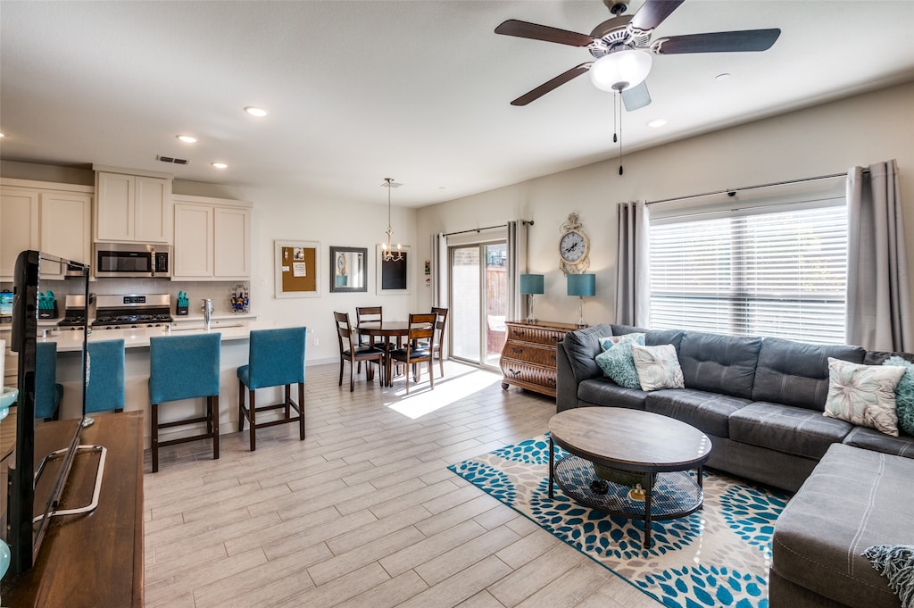 living room featuring light hardwood / wood-style flooring, a healthy amount of sunlight, and ceiling fan with notable chandelier