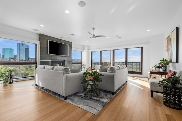 living room with ceiling fan, a healthy amount of sunlight, light hardwood / wood-style floors, and a tile fireplace