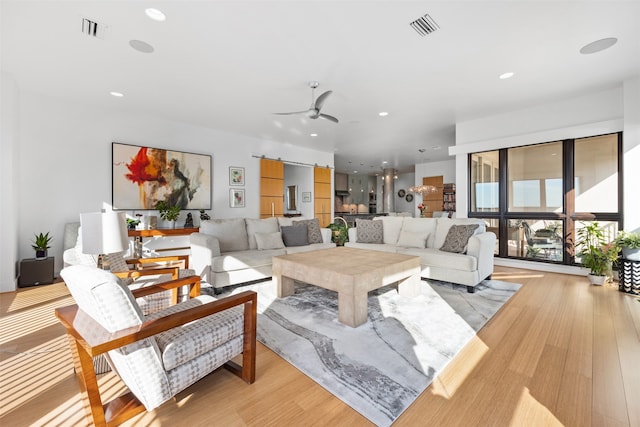 living room with a barn door, ceiling fan, and light hardwood / wood-style floors