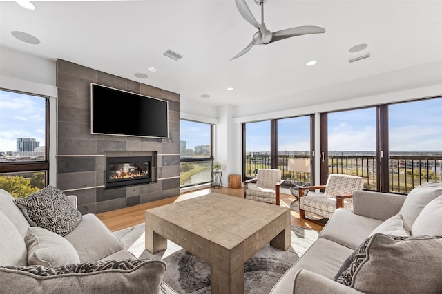 living room with a tiled fireplace, ceiling fan, and light wood-type flooring