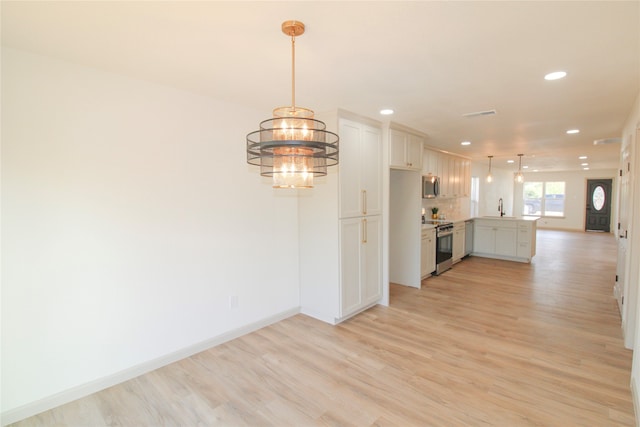 kitchen with appliances with stainless steel finishes, light wood-type flooring, hanging light fixtures, and sink