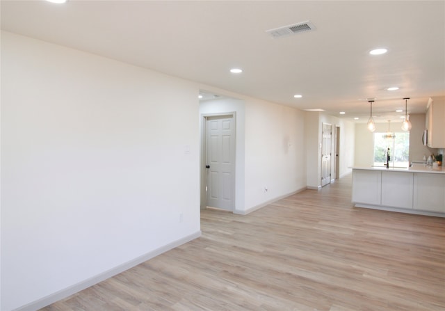 interior space with white cabinetry, sink, light hardwood / wood-style floors, and decorative light fixtures