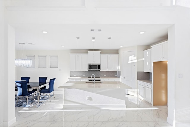 kitchen with pendant lighting, white cabinetry, sink, backsplash, and a center island with sink