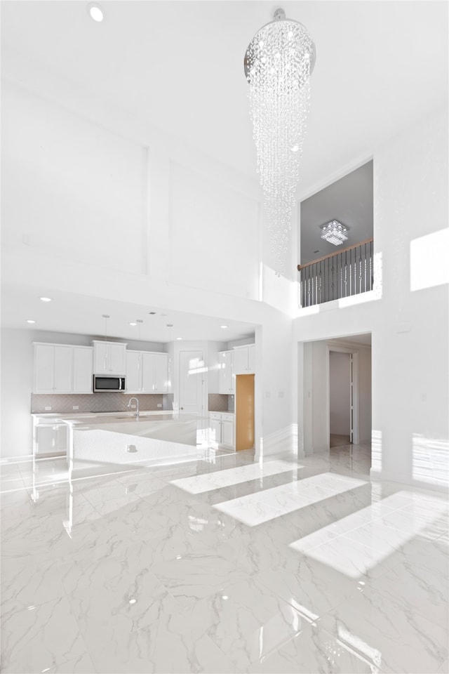 unfurnished living room with a notable chandelier, a towering ceiling, and sink