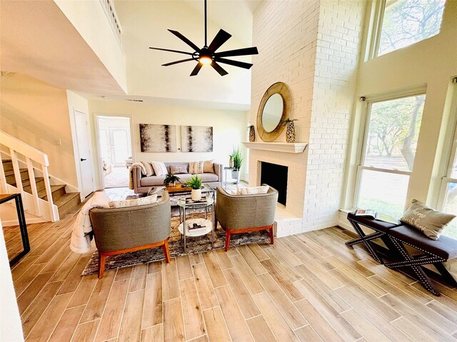 living room featuring wood-type flooring, a brick fireplace, ceiling fan, and a high ceiling