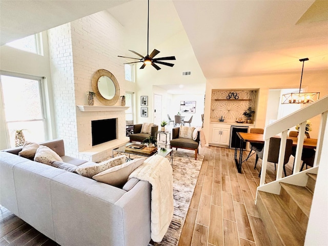 living room featuring a fireplace, wood-type flooring, ceiling fan with notable chandelier, and high vaulted ceiling