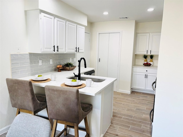 kitchen with white cabinets, a kitchen breakfast bar, sink, decorative backsplash, and kitchen peninsula