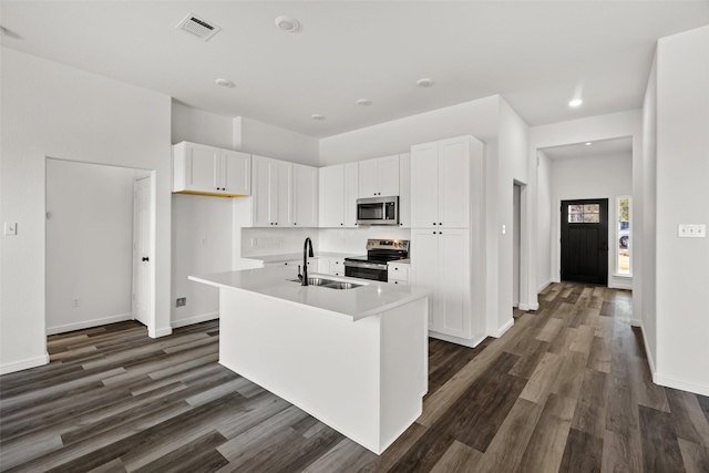 kitchen featuring dark wood-type flooring, a center island with sink, sink, appliances with stainless steel finishes, and white cabinetry