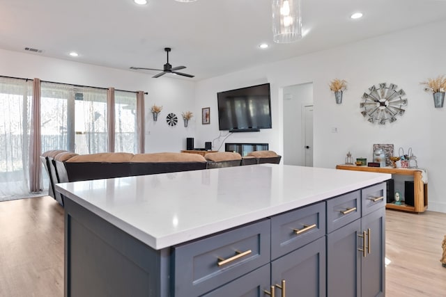 kitchen featuring hanging light fixtures, ceiling fan, a center island, and light hardwood / wood-style floors