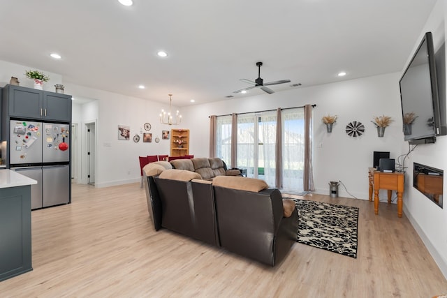 living room featuring ceiling fan with notable chandelier and light hardwood / wood-style flooring