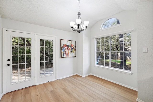 unfurnished dining area featuring a chandelier, vaulted ceiling, light hardwood / wood-style flooring, and a textured ceiling