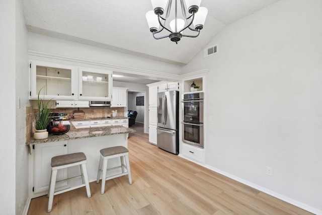 kitchen featuring white cabinetry, stainless steel appliances, a kitchen breakfast bar, decorative light fixtures, and kitchen peninsula