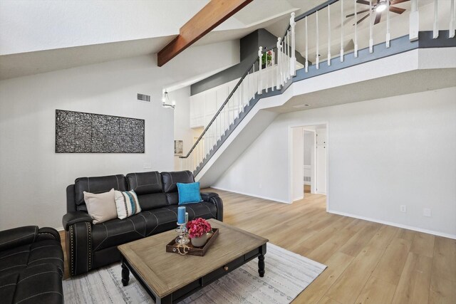 living room with ceiling fan, beam ceiling, light wood-type flooring, and a high ceiling