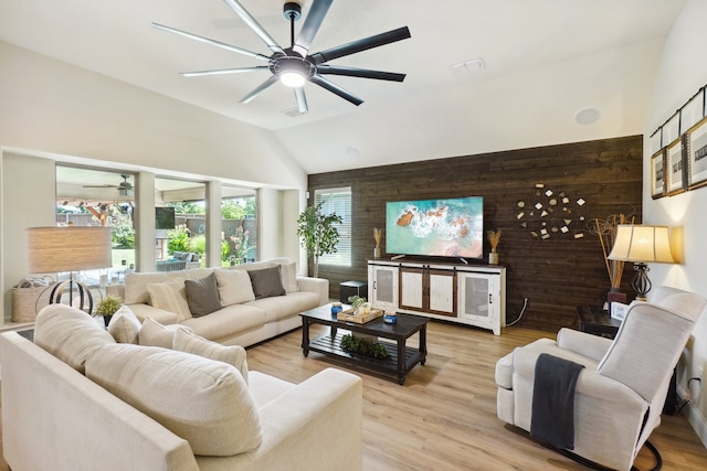 living room with light wood-type flooring, ceiling fan, lofted ceiling, and wood walls