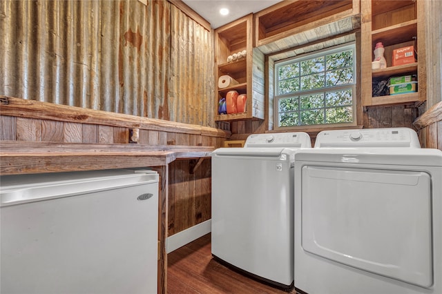 clothes washing area featuring washer and clothes dryer, wooden walls, dark wood finished floors, and laundry area