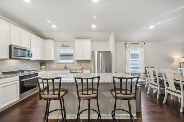 kitchen featuring a center island, light stone counters, stainless steel appliances, and dark wood-type flooring