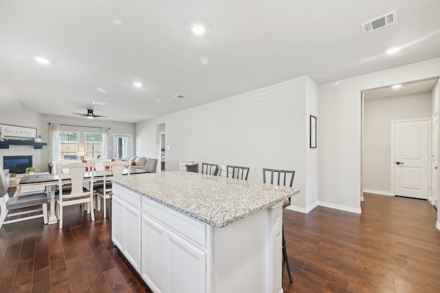 kitchen featuring light stone countertops, a center island, dark hardwood / wood-style floors, white cabinetry, and a breakfast bar area