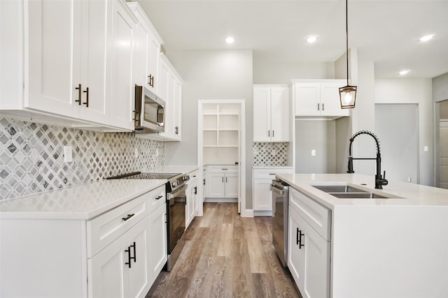 kitchen with hanging light fixtures, white cabinets, stainless steel appliances, and light wood-type flooring