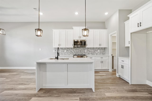 kitchen with pendant lighting, light hardwood / wood-style floors, white cabinets, and a kitchen island with sink